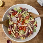 Gordon Ramsay chopped salad: shredded romaine and radicchio with cherry tomatoes, red pepper, chickpeas, Edam matchsticks and salami strips, dried oregano on top, in a big bowl