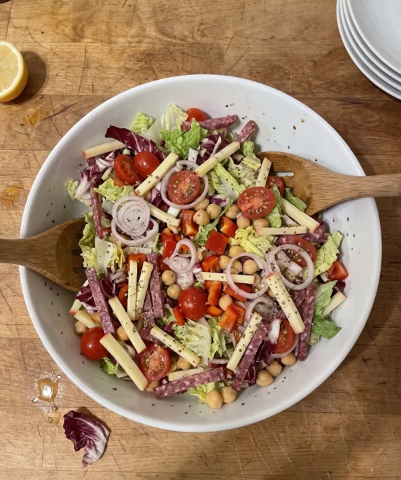 Gordon Ramsay chopped salad: shredded romaine and radicchio with cherry tomatoes, red pepper, chickpeas, Edam matchsticks and salami strips, dried oregano on top, in a big bowl