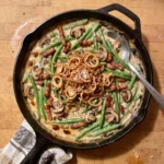 Gordon Ramsay green bean casserole with bacon: green beans and mushrooms in a creamy sauce topped with crispy fried shallots in a skillet