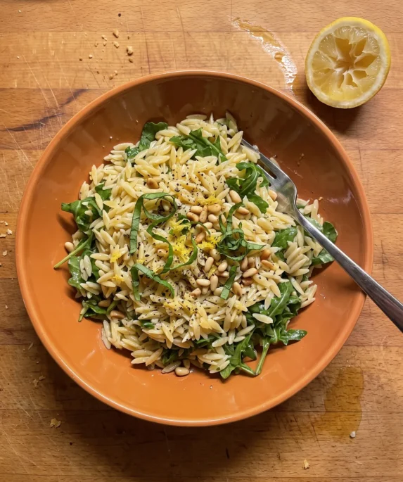 Gordon Ramsay orzo pasta salad with lemon and Parmesan dressing, arugula, basil and toasted pine nuts in a bowl