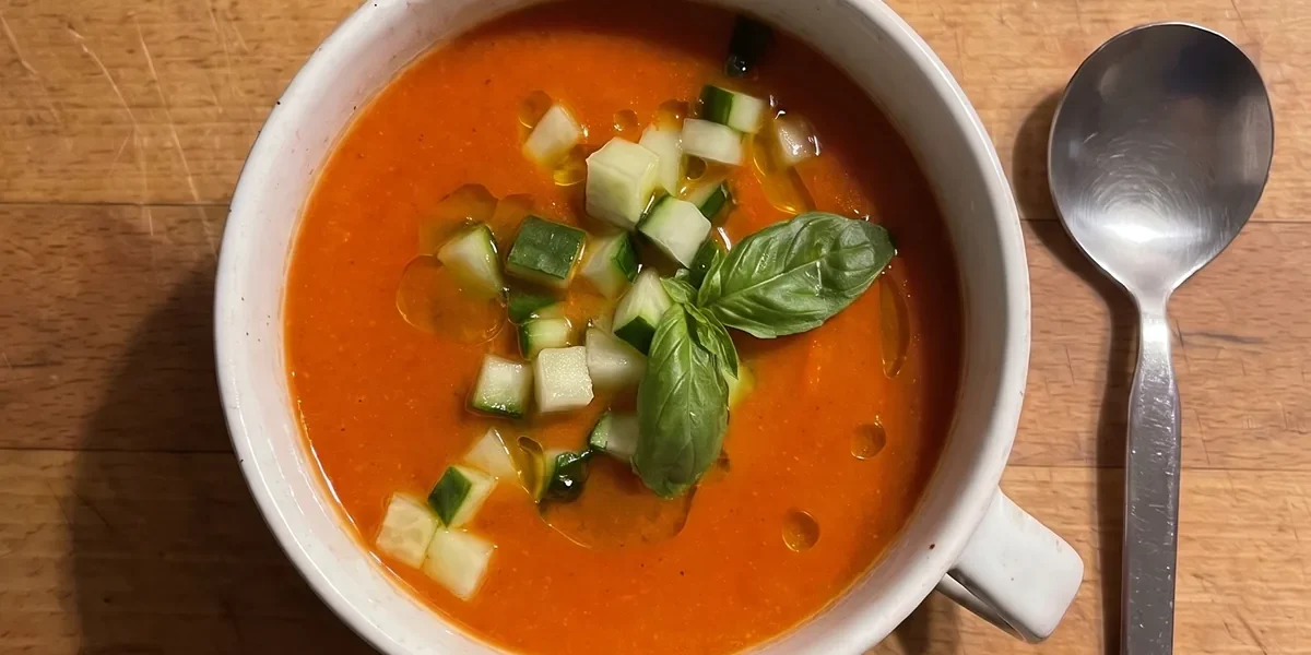 Gordon Ramsay roasted red pepper and tomato soup: chilled orange-red soup in a white soup cup topped with diced cucumber, a basil sprig and olive oil