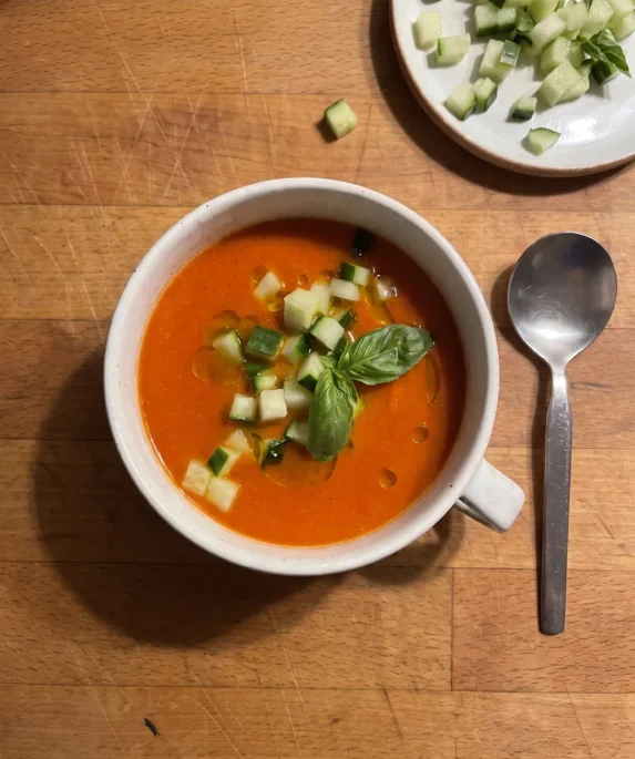 Gordon Ramsay roasted red pepper and tomato soup: chilled orange-red soup in a white soup cup topped with diced cucumber, a basil sprig and olive oil