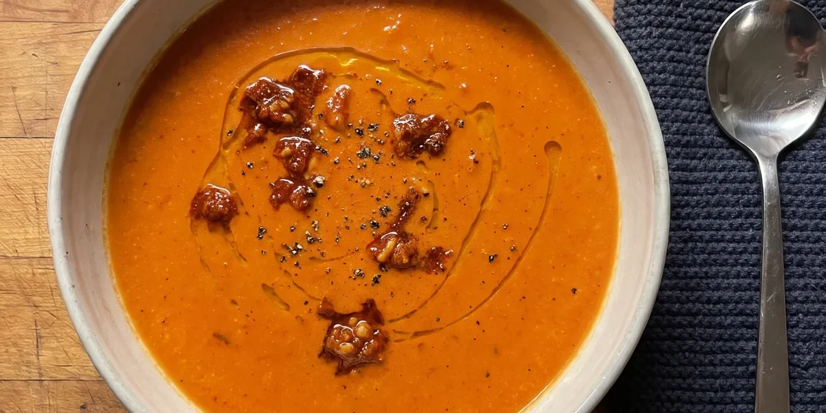 Gordon Ramsay roasted tomato soup: a bowl of creamy orange-red tomato soup topped with spoonfuls of sun-dried tomato pesto and a swirl of olive oil