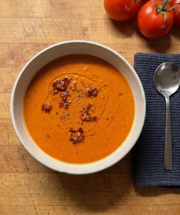 Gordon Ramsay roasted tomato soup: a bowl of creamy orange-red tomato soup topped with spoonfuls of sun-dried tomato pesto and a swirl of olive oil