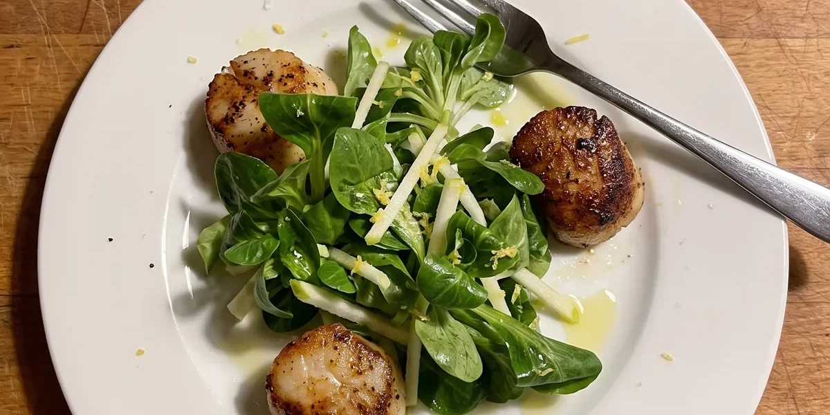 Gordon Ramsay scallop salad: golden seared scallops around a pile of lamb's lettuce and Granny Smith apple matchsticks with lemon zest on a white plate