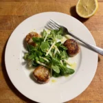 Gordon Ramsay scallop salad: golden seared scallops around a pile of lamb's lettuce and Granny Smith apple matchsticks with lemon zest on a white plate