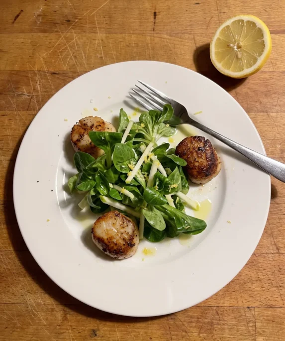 Gordon Ramsay scallop salad: golden seared scallops around a pile of lamb's lettuce and Granny Smith apple matchsticks with lemon zest on a white plate