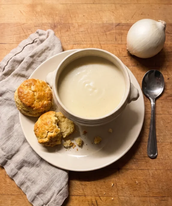 Gordon Ramsay white onion soup: a handled bowl of smooth pale onion and cheddar soup with two warm scones on the plate